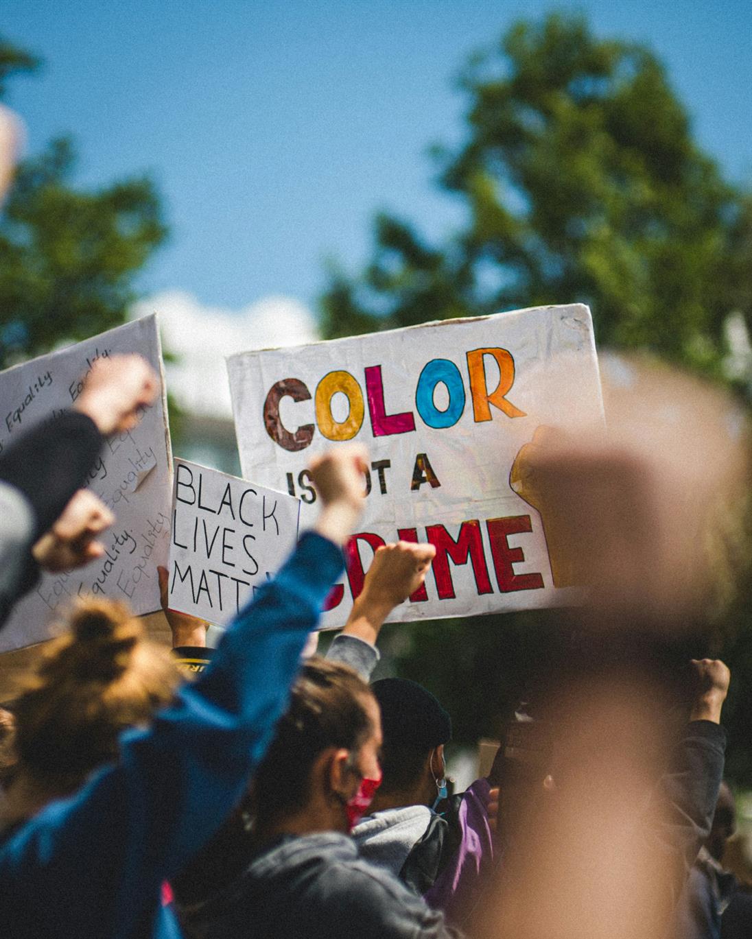 Eine Aufnahme von Menschen bei einer Demonstration. Der Fokus liegt auf zwei Schildern, die in die Luft gehalten werden und folgende Aussagen zeigen: "Black lifes matter" und "Color is not a crime"